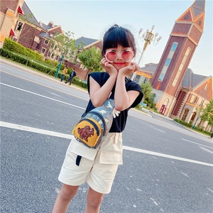Outdoor shot of a little girl wearing a green dinosaur print chest bag with yellow patch