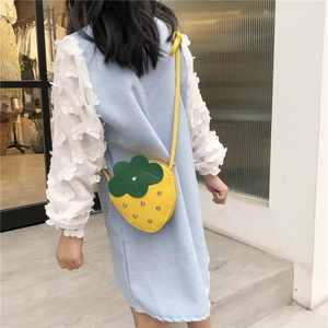 Detail view of a yellow strawberry kids crossbody bag with green leaf decor and silver studs