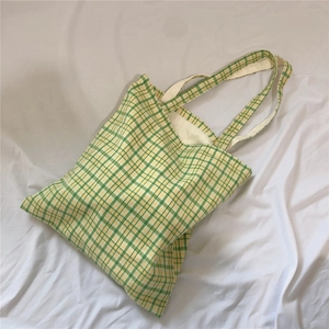 Detailed top view of a yellow and green checkered canvas tote bag on soft white fabric