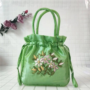Detail of green satin handbag featuring floral embroidery and drawstring closure