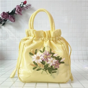 Detail of yellow satin bucket bag featuring intricate ribbon embroidery and drawstring