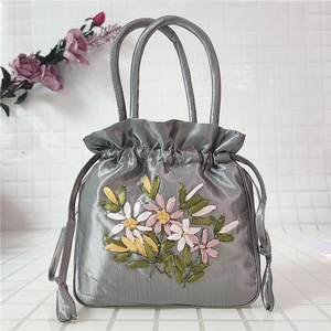 Detailed close-up of ribbon floral embroidery on silk satin drawstring handbag