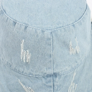 Close-up of distressed edges and frayed hole detail on a light blue denim bucket hat