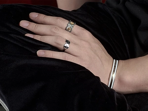 Close-up of stacked jewelry featuring a sunflower ring and an enamel rose gold bracelet