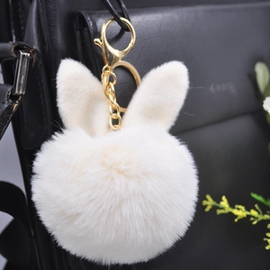 Cute white plush bunny ear pompom keychain with gold hardware on a black handbag