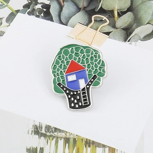 Artistic tree house enamel pin brooch with green canopy and red roof on a card