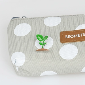 Close-up of a green seedling sprout pin badge attached to a grey polka dot fabric bag