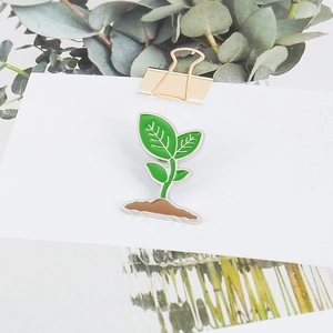 Close-up of creative green plant and brown soil enamel brooch on white card