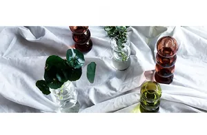 Détail de vases en verre à bulles empilés en ambre et vert sur lin blanc