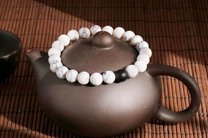 White turquoise beaded bracelet with one black matte bead displayed on a ceramic teapot