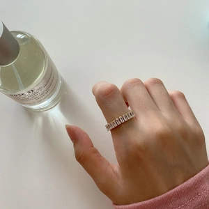 Detail of a gold-plated ring with rectangular zircon stones worn next to a perfume bottle