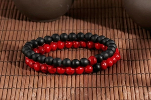 Macro detail of matte black and red stone beaded bracelets on dark bamboo mat