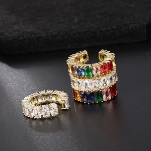 Dettaglio macro di ear cuff dorato con pietre di zircone colorate su sfondo nero opaco