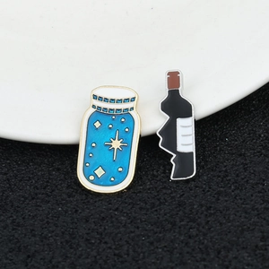 Macro shot of blue starry bottle and black wine bottle enamel pins on a dark textured surface