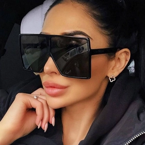 Close-up of oversized square black sunglasses worn by model in a car interior