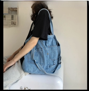 Side view of a vintage wash denim shoulder bag with multiple functional flap pockets