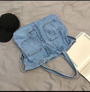 Detail of light blue denim tote bag featuring dual front pockets and metal buckle closure