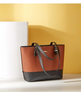 Detail view of two-tone brown and black PU leather tote bag with metal bar on white platform