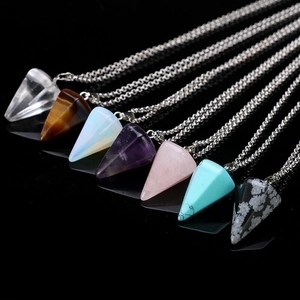 Macro detail of various natural gemstone pendulum pendants on silver chains over dark surface
