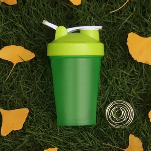 Detail of green sports protein shaker bottle with stainless steel mixing ball on grass