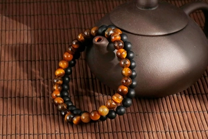 Detail of natural tiger eye and matte black agate beaded bracelets on ceramic vessel