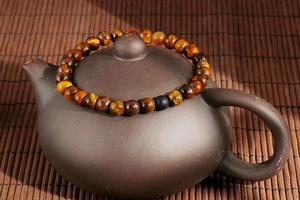 Macro shot of tiger eye stone beads on a clay teapot lid with warm lighting