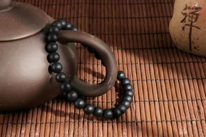 Matte black agate beaded bracelet displayed on a purple clay teapot in a Zen setting