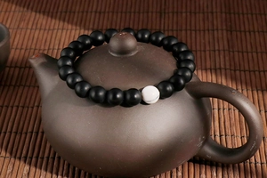 Minimalist black beaded bracelet with a white turquoise accent on a bamboo mat