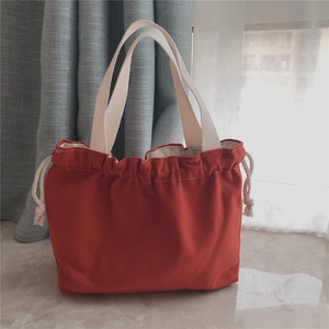 Detail of red canvas tote bag with drawstring closure and cream-colored woven handles