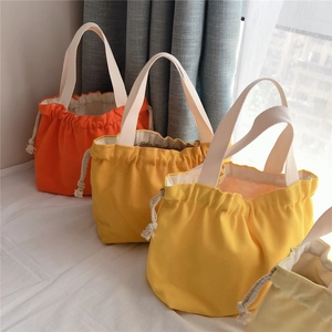 Detailed view of drawstring canvas handbags in orange and yellow with cotton rope closure