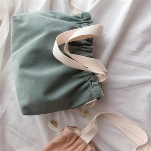 Close-up of sage green and apricot canvas drawstring handbags with cotton strap handles