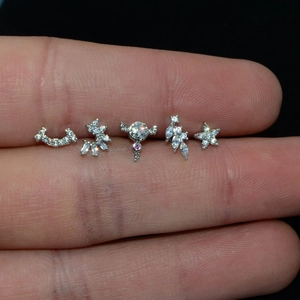 Close-up of five mini silver piercing studs with cubic zirconia in star and floral shapes