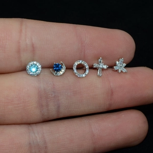 Detail of five mini silver stud earrings with blue stones and zircon on a hand