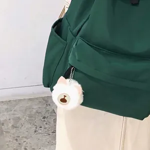 Cute white plush teddy bear pompom keychain charm on a dark green backpack