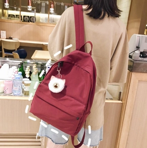 Close-up of red nylon backpack featuring a white plush pom-pom and cute teddy bear charm