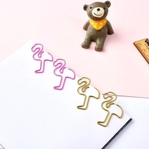 Pink and gold flamingo shaped paper clips on a white notebook with a pastel background