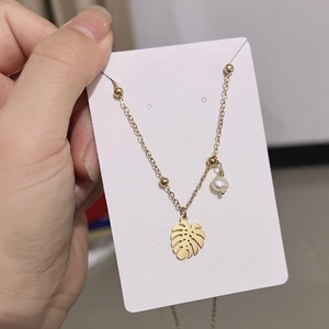 Detail view of gold necklace featuring monstera leaf pendant, pearl and beads accents