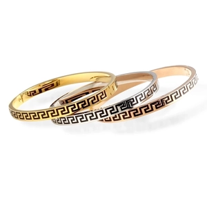 Close-up of three metal bangles in gold, silver, and rose gold with black fret patterns