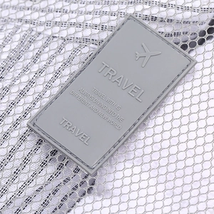 Close-up detail of grey mesh travel storage bag with stylish rubber logo patch and durable texture.