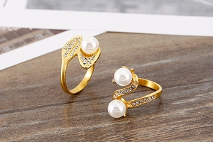 Macro shot of gold-plated rings with white pearls and small diamonds on a wood surface
