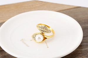 Macro detail of gold-plated open ring featuring leaves, a pearl, and sparkling rhinestones