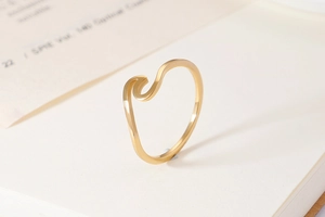 Minimalist gold wave ring elegantly displayed on open book pages with natural lighting