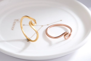 Detailed close-up of wave-shaped rings in gold and rose gold with matte brushed finish