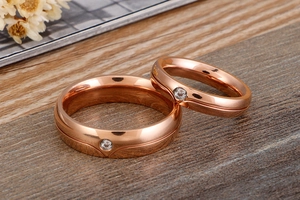 Macro shot of rose gold couple rings featuring single diamond inlay on wood background