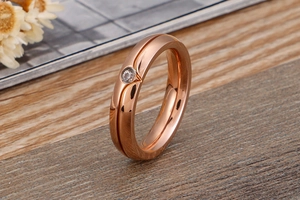 Detailed view of rose gold titanium ring with a centered diamond on warm wood surface