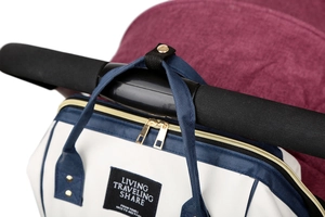 Close-up of a stylish diaper bag with metal zippers hanging on a stroller handlebar