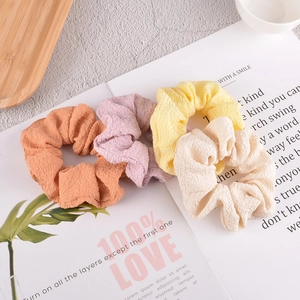 Detail of four colorful seersucker scrunchies in orange, purple, yellow, and beige colors