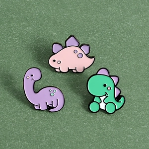 Détail de pins dinosaures mignons en émail coloré rose, violet et vert sur fond vert