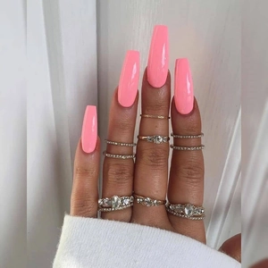 Primer plano de uñas postizas largas rosadas y conjunto de anillos con pedrería