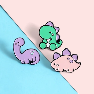 Détail de trois épinglettes de dinosaures colorés en émail sur fond bicolore pastel
